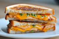 Grilled cheese sandwich with melted cheddar on toasted white bread, garnished with fresh herbs, stacked in layers on white plate, close up view of gooey texture.
