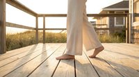 Woman walking barefoot on wooden deck during golden hour sunset creating peaceful relaxation moment for wellness and mindfulness concepts.
