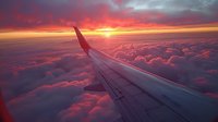 Dramatic sunset view from airplane window over fluffy clouds with aircraft wing silhouette, perfect for travel advertising, aviation business, or wanderlust inspiration backgrounds.
