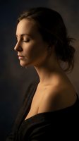 Serene young woman in profile with closed eyes and dramatic lighting wearing black garment against dark moody background for wellness and meditation concepts.