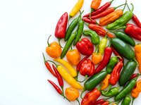 Colorful assortment of fresh hot chili peppers in red, green, yellow and orange varieties scattered on white background for culinary and cooking themes.