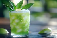 Fresh green cocktail with crushed ice and tropical leaves garnish in glass on wooden table, selective focus on condensation droplets and bright lighting.