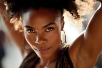 Close-up portrait of confident African American woman with natural curly hair and hoop earrings, illuminated by warm backlighting creating a glowing effect.