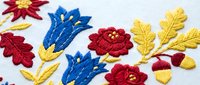 Colorful hand embroidery with red flowers, blue tulips, and golden leaves on white fabric, showcasing traditional folk textile art.
