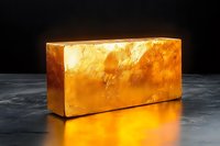 Glowing golden bar on dark background with bright reflection on concrete surface, precious metal investment concept for financial and banking sector.