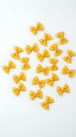 Yellow farfalle pasta isolated on white background, arranged in scattered pattern. Suitable for food photography, cooking blogs, recipe design, and culinary marketing materials.