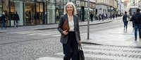 Professional blonde businesswoman walking confidently through modern city street with briefcase, representing corporate success and urban lifestyle.