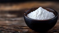 White powder ingredient in black ceramic bowl on rustic wooden table with shallow depth of field, dark moody food photography style.