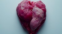 Fresh raw beef heart shaped like anatomical heart on light blue background, dramatic lighting creates moody atmosphere for culinary or medical concept.