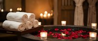 Luxury spa bathtub with red rose petals, rolled towels and candles creating romantic wellness atmosphere for relaxation and self-care rituals.