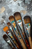 Used paintbrushes with colorful paint stains arranged on textured gray background, showing artistic tools with orange and turquoise paint splatters and natural wear.