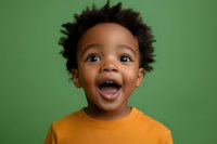 Joyful African American toddler boy with curly hair wearing orange t-shirt expressing pure happiness and excitement against green studio background.