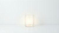 Glowing candle in a clear glass holder on a white surface, soft warm light, minimalist style, cozy ambiance for home decor concepts.