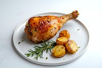 Roasted chicken leg with crispy golden skin served on white plate with baby potatoes and fresh rosemary sprig, photographed on light marble background.
