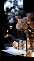 Romantic evening setup with pink roses in crystal vase, empty cocktail glass and document on table against blurred city lights background. Moody restaurant ambiance.
