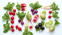 Fresh colorful radishes with green leaves arranged on white background. Organic root vegetables including red, purple, white varieties for healthy cooking.