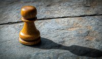Wooden chess pawn casting dramatic shadow on textured stone surface, symbolizing strategy, leadership and personal growth in business concepts.