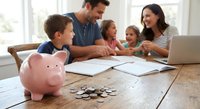 Happy family with children learning about money management and savings at home with piggy bank and coins on wooden table.