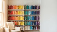Rainbow colored books arranged by hue on white bookshelf creating vibrant spectrum display in modern reading nook with cozy armchair and natural window light.