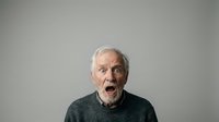 Senior man with white hair and Caucasian ethnicity expressing shock or surprise with open mouth against neutral gray background for portrait and emotion stock use.