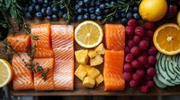 Fresh salmon fillets arranged with citrus slices, raspberries, blueberries and herbs on wooden board. Healthy omega-3 rich seafood and antioxidant fruits composition.