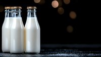 Fresh milk bottles on dark surface with warm bokeh lights creating cozy atmosphere for dairy product advertising and healthy lifestyle campaigns.