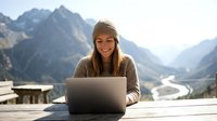 Young woman working on laptop computer outdoors with mountain landscape background. Remote work lifestyle concept for digital nomad and freelancer.