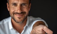 Confident mature Hispanic businessman with salt and pepper beard wearing white shirt smiles warmly against dark background, conveying trust and leadership.