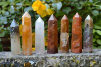 Collection of colorful healing crystal points arranged outdoors with natural foliage background for meditation and spiritual wellness practices.