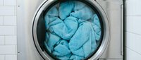Blue towels and linens loaded in modern washing machine drum ready for laundry cycle in clean white tiled bathroom interior.