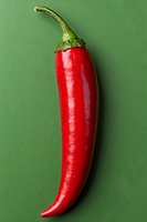 Fresh red chili pepper with green stem isolated on green background, minimalist food photography composition for culinary and spicy food concepts.