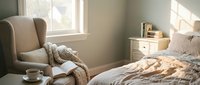 Cozy bedroom interior with comfortable armchair, soft bedding and natural sunlight streaming through window creating warm peaceful atmosphere.