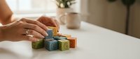 Woman hands arranging colorful wooden alphabet blocks on white table in cozy home interior with Christmas tree background for early learning.
