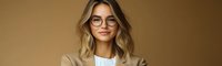 Young professional woman with blonde wavy hair wearing eyeglasses and beige blazer smiling confidently against brown background, modern business portrait.