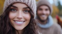 Young woman with bright smile wearing knit beanie outdoors in autumn, with blurred male figure in background. Natural lifestyle portrait capturing genuine happiness.