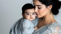 Young mother in elegant silver lace dress tenderly embracing baby in matching outfit against light background, expressing maternal love and gentle care in soft lighting.