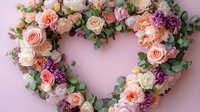 Romantic heart-shaped floral wreath with pink, peach roses, purple carnations and eucalyptus leaves on soft pink background for wedding or Valentine's day decoration.