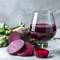 Fresh beetroot juice in wine glass with whole and sliced beets on marble surface, surrounded by green leaves for healthy detox drinks.