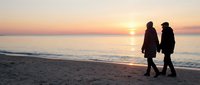 Romantic couple silhouettes walking on beach at golden sunset with calm ocean waves and warm sky colors creating peaceful evening atmosphere.