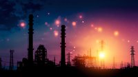 Industrial refinery silhouettes against dramatic sunset sky with power lines and glowing bokeh lights creating atmospheric evening landscape.