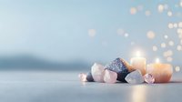 Healing crystals and glowing candles on soft blue background with bokeh lights create serene spiritual atmosphere for meditation and wellness practices.
