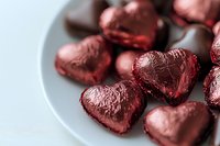 Red foil wrapped chocolate hearts on white plate for Valentine's Day romantic celebration and love themed confectionery treats.