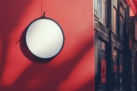 Round white signboard on vibrant red wall with dramatic shadows, urban storefront setting for business branding and street photography.