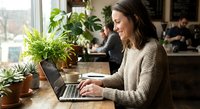 Young woman working on laptop at home office desk surrounded by green plants creating productive workspace atmosphere for remote work and freelancing.