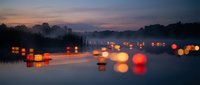 Floating lanterns illuminate calm water at twilight creating magical reflections during peaceful evening ceremony with warm glowing lights across serene lake surface.