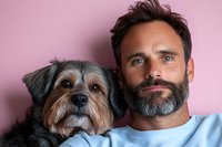 Mature Caucasian bearded man with mixed breed terrier dog posing together against pink background, showing bond between pet owner and companion animal.