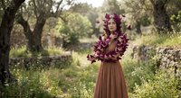 Young woman with purple floral crown and brown dress standing in natural outdoor setting with trees and greenery for lifestyle photography.