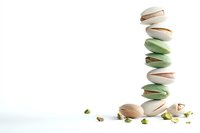 Stack of green and white macarons with pistachios scattered around on white background, minimalist food photography composition for pastry marketing.