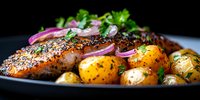 Grilled salmon fillet with poppy seeds, baby potatoes and red onions garnished with fresh herbs on black plate, close up panoramic view in dark setting.
