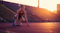 Athletic young woman in starting position on running track during golden hour sunset at stadium ready to sprint.